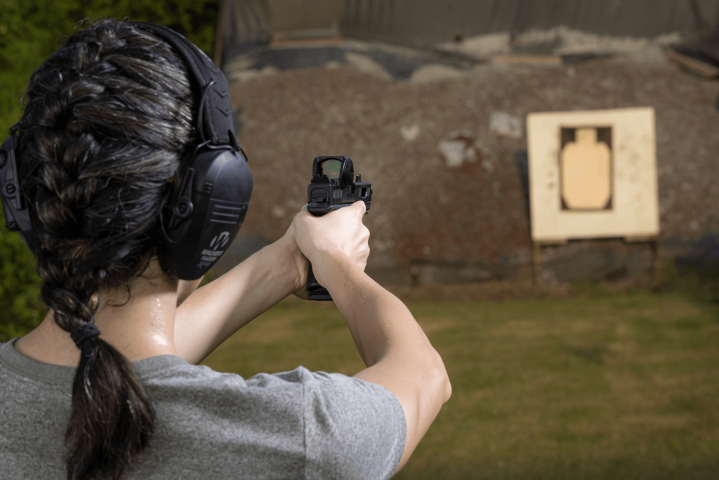 Behind the back view of a woman aiming her pistol at a target at an outdoor shooting range