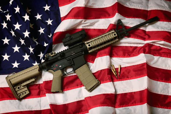 AR15 sitting on top of an American flag, three bullets sit next to the weapon