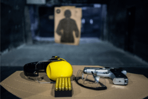 firearm, protective gear, and ammunition sit on a wooden countertop at an indoor gun range