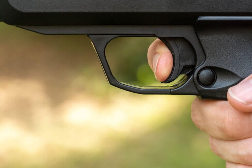 Close up view showing a hand holding a pistol with a finger on the trigger