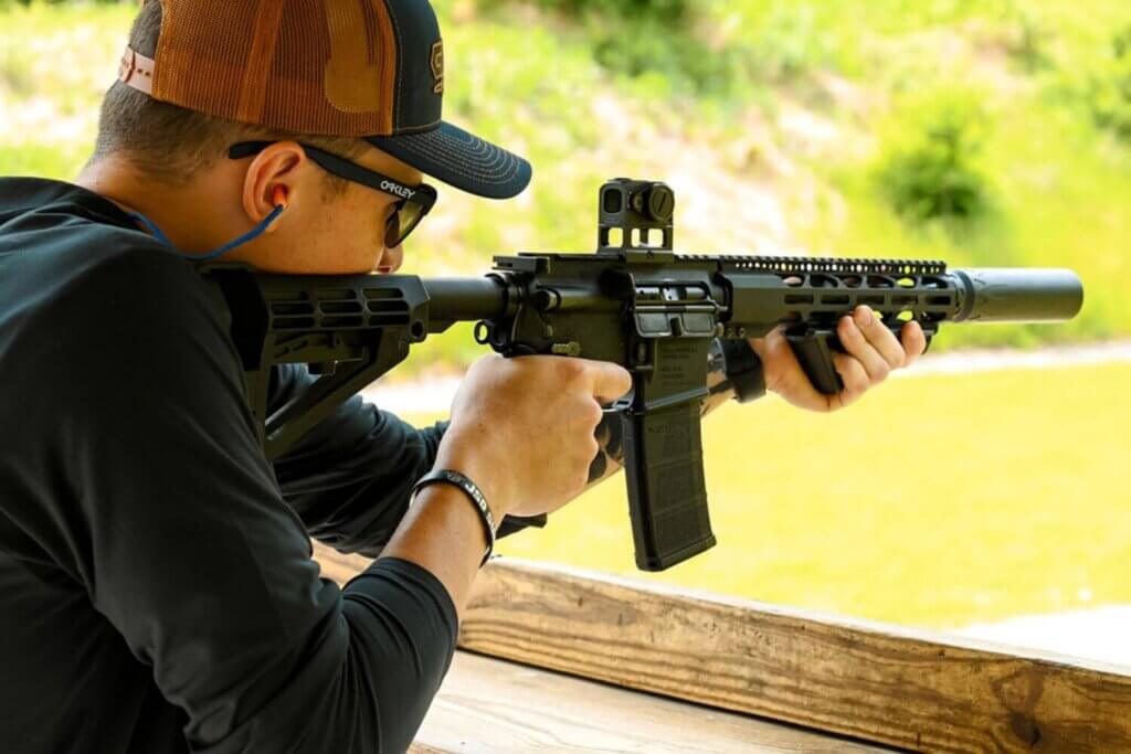 Man at an outdoor shooting range shooting an AR-15 with a Gideon Optics Mediator mounted