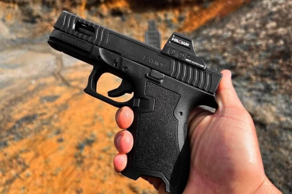Hand holding a pistol with an aftermarket slide and a red dot sight mounted