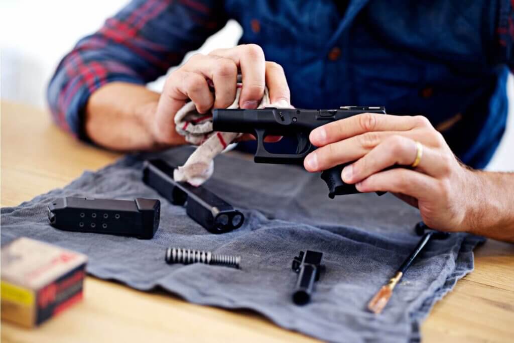 Man sitting at a table with a gun and supplies to clean it