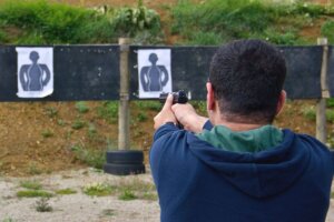 Man wearing a blue and green hoodie at an outdoor shooting range practicing with a pistol