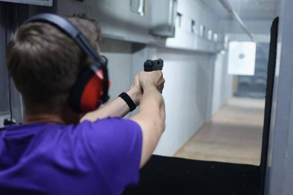 Man wearing red ear protection while holding a pistol at an indoor shooting range