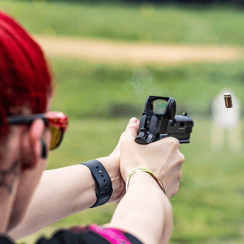 woman with red hair shooting a firearm at an outdoor range
