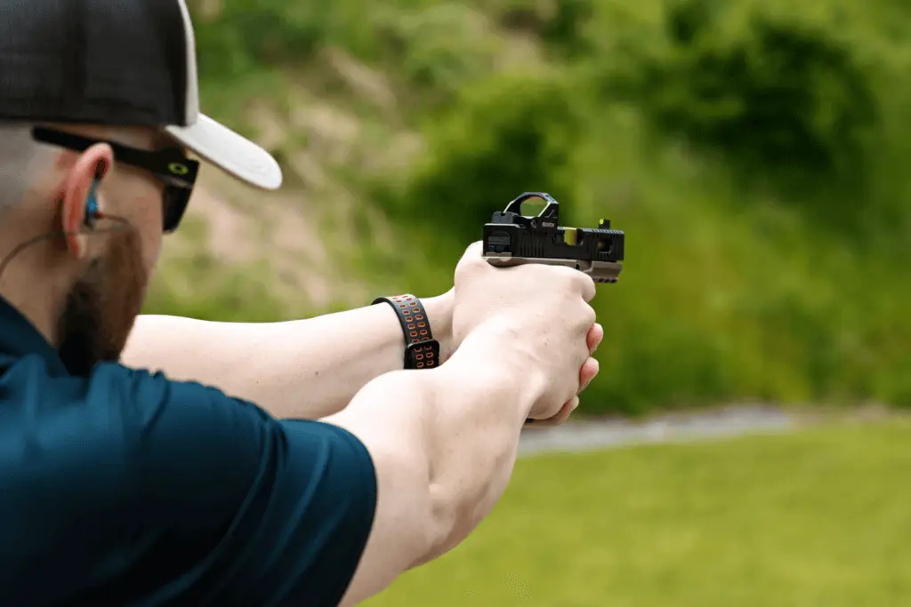 Man at an outdoor shooting range wearing protective gear is shooting a pistol