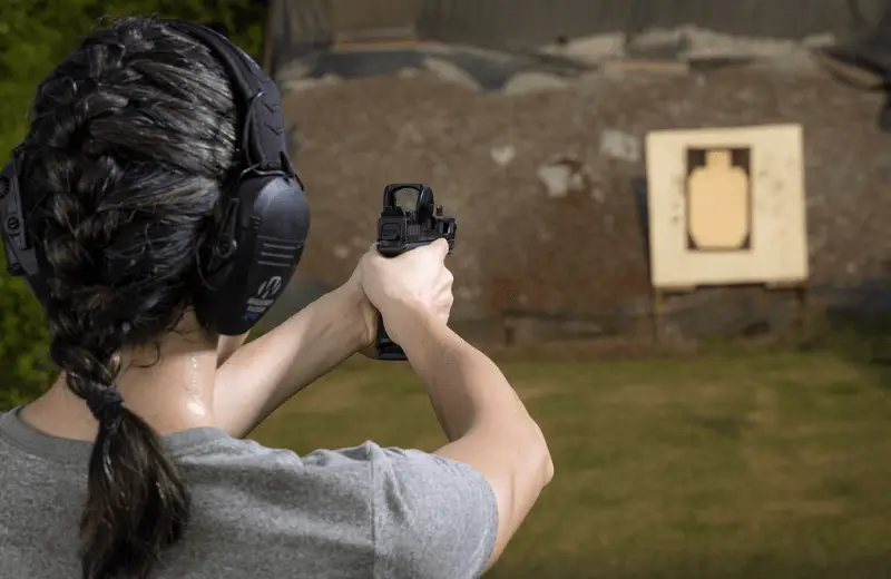 woman at an outdoor shooting range aiming her pistol at a target