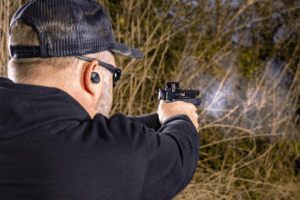 Behind the back view of a man firing a pistol at an outdoor shooting range