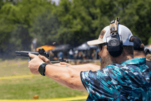 Man wearing protective eyewear and earwear firing a pistol at an outdoor shooting competition