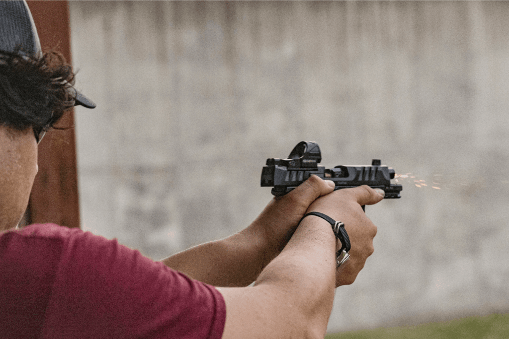Man at an outdoor shooting range firing a pistol with a red dot mounted